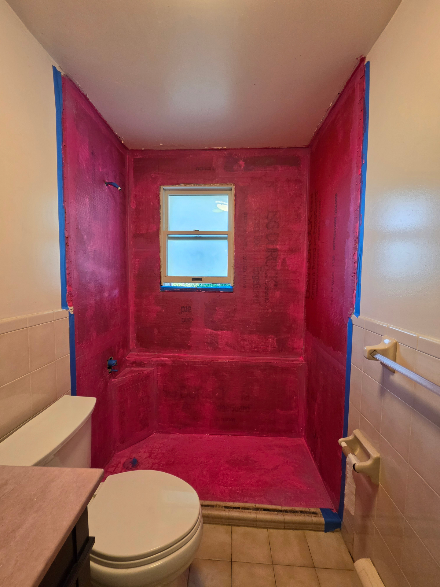 Shower alcove fully coated with pink waterproofing membrane over cement board before tiling, NYC bathroom renovation