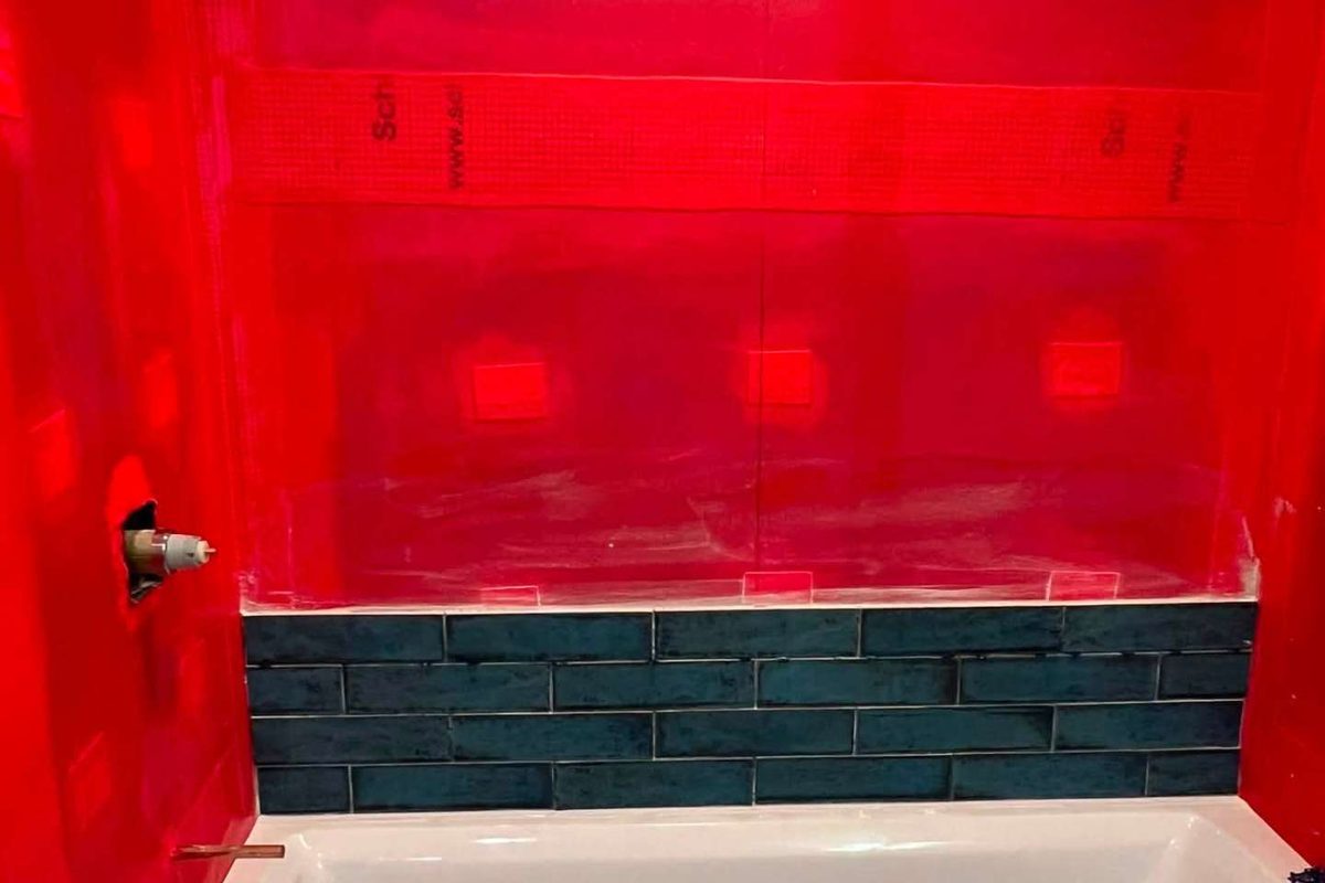 Before: Bronx bathroom remodel in progress with red waterproofing membrane over the tub and the first row of teal subway tile set in Morris Park