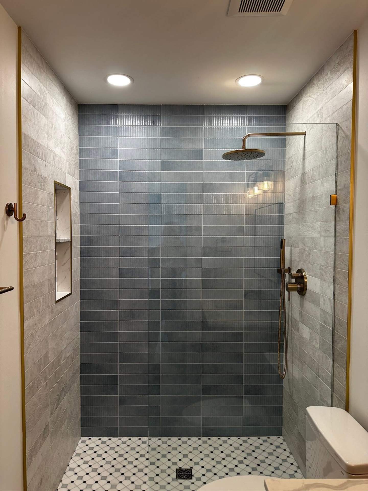 Frameless glass walk-in shower with blue stacked tile and mosaic floor, NYC bathroom renovation