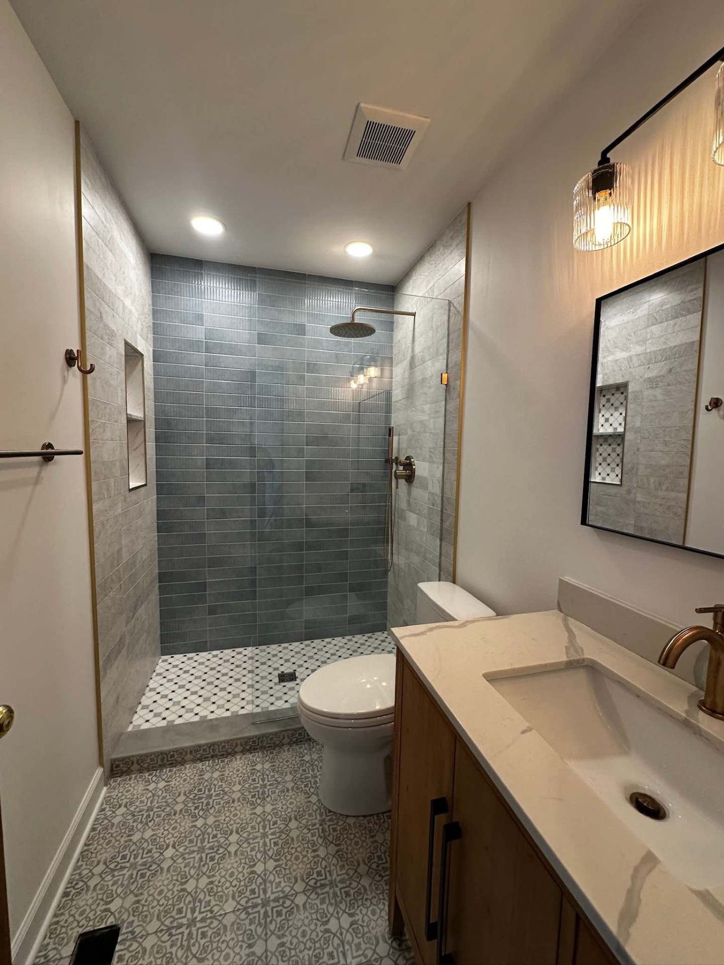 Completed NYC bathroom with blue fluted tile shower, patterned floor tile, wood vanity and quartz top