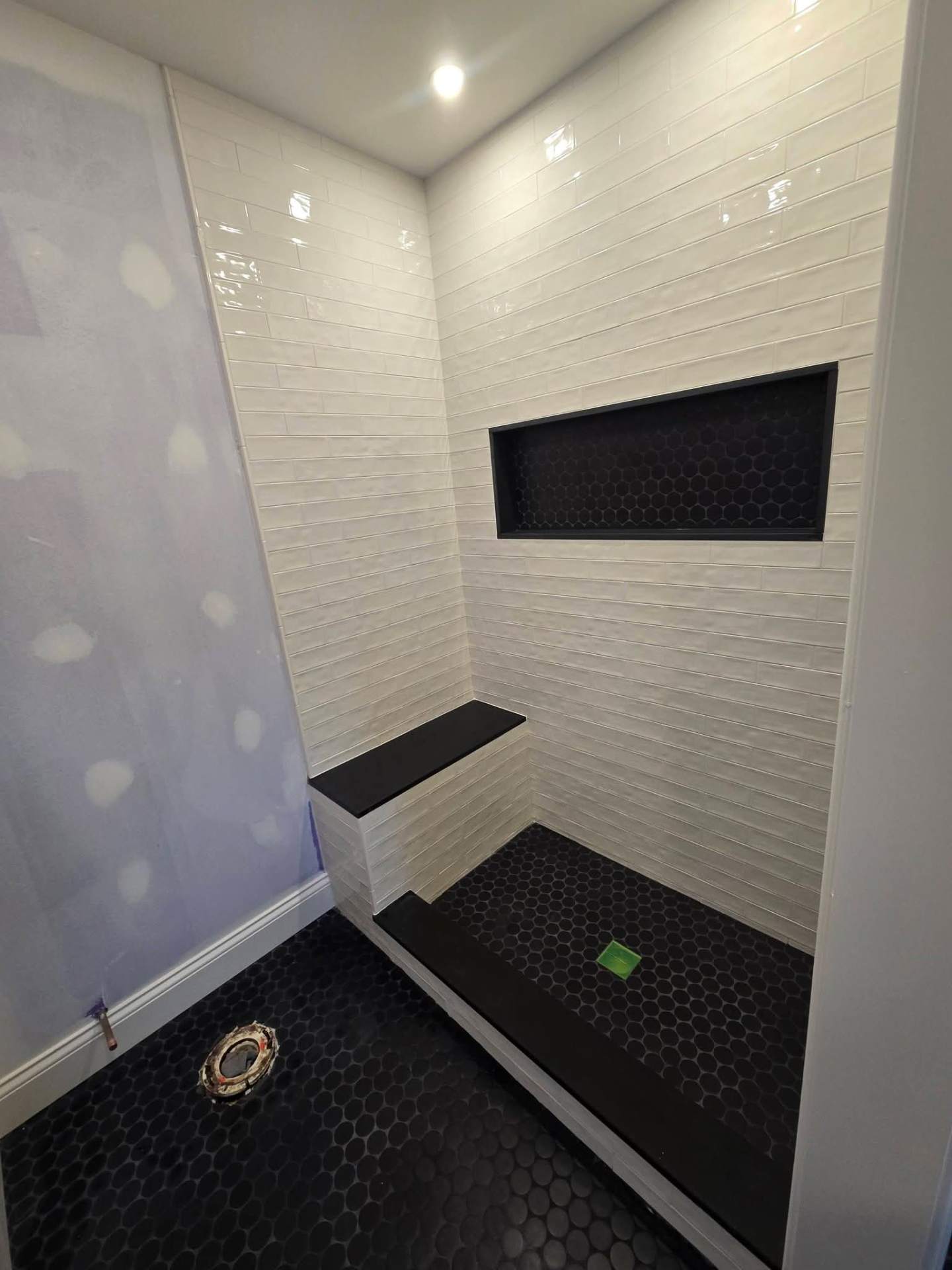 Walk-in shower with white subway tile, black hexagon floor, built-in bench and long black niche, NYC bathroom renovation