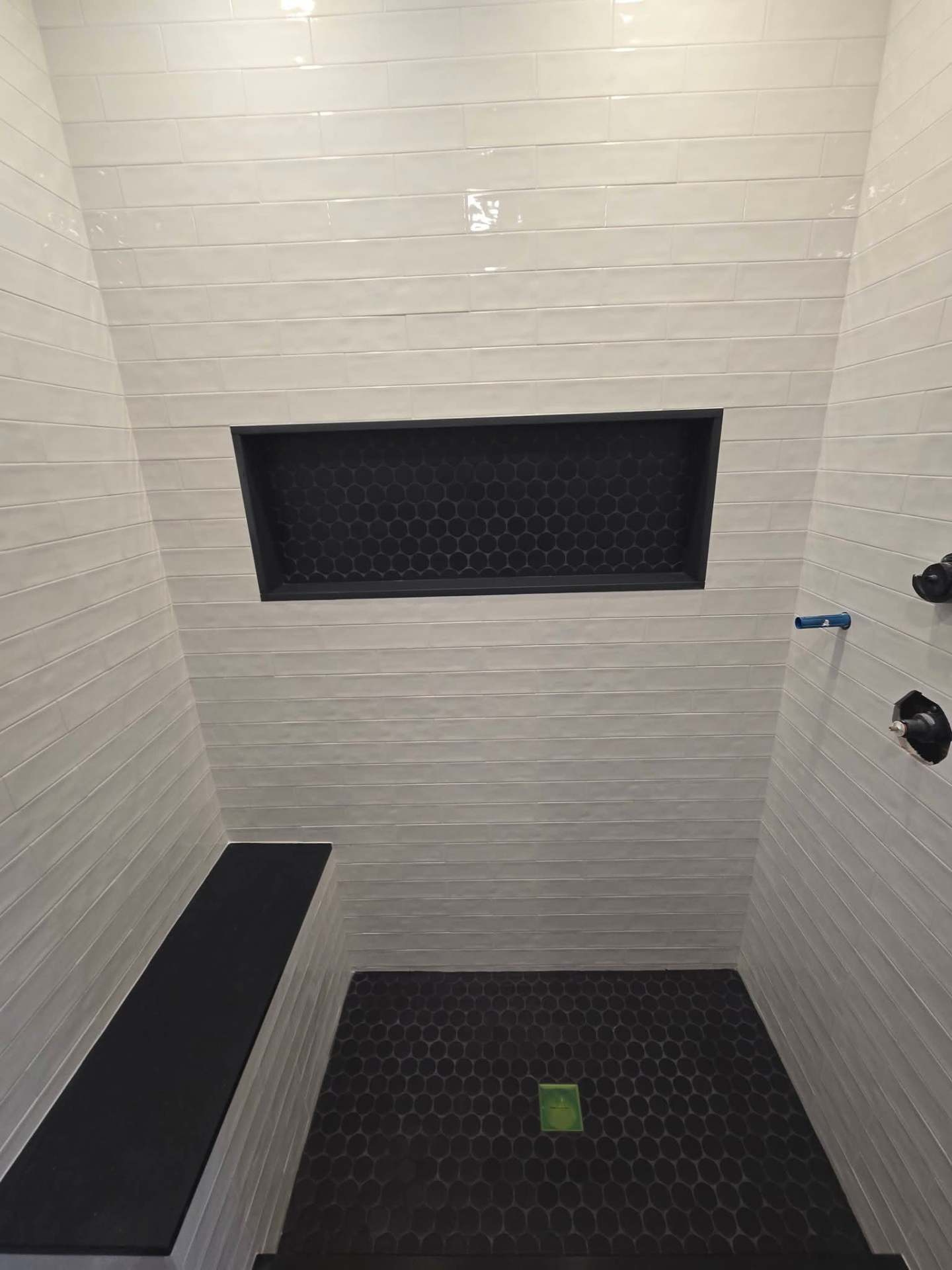 White tiled shower with black penny-tile niche, bench seat and hexagon floor, NYC bathroom renovation