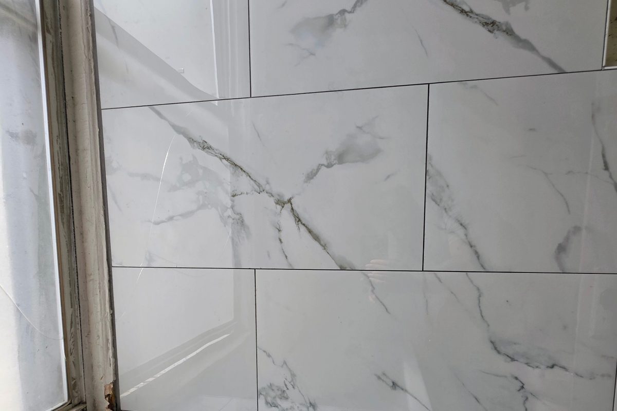 Before: large-format marble-look porcelain tile being installed on the wall and tub deck of a Pelham Bay Bronx bathroom renovation
