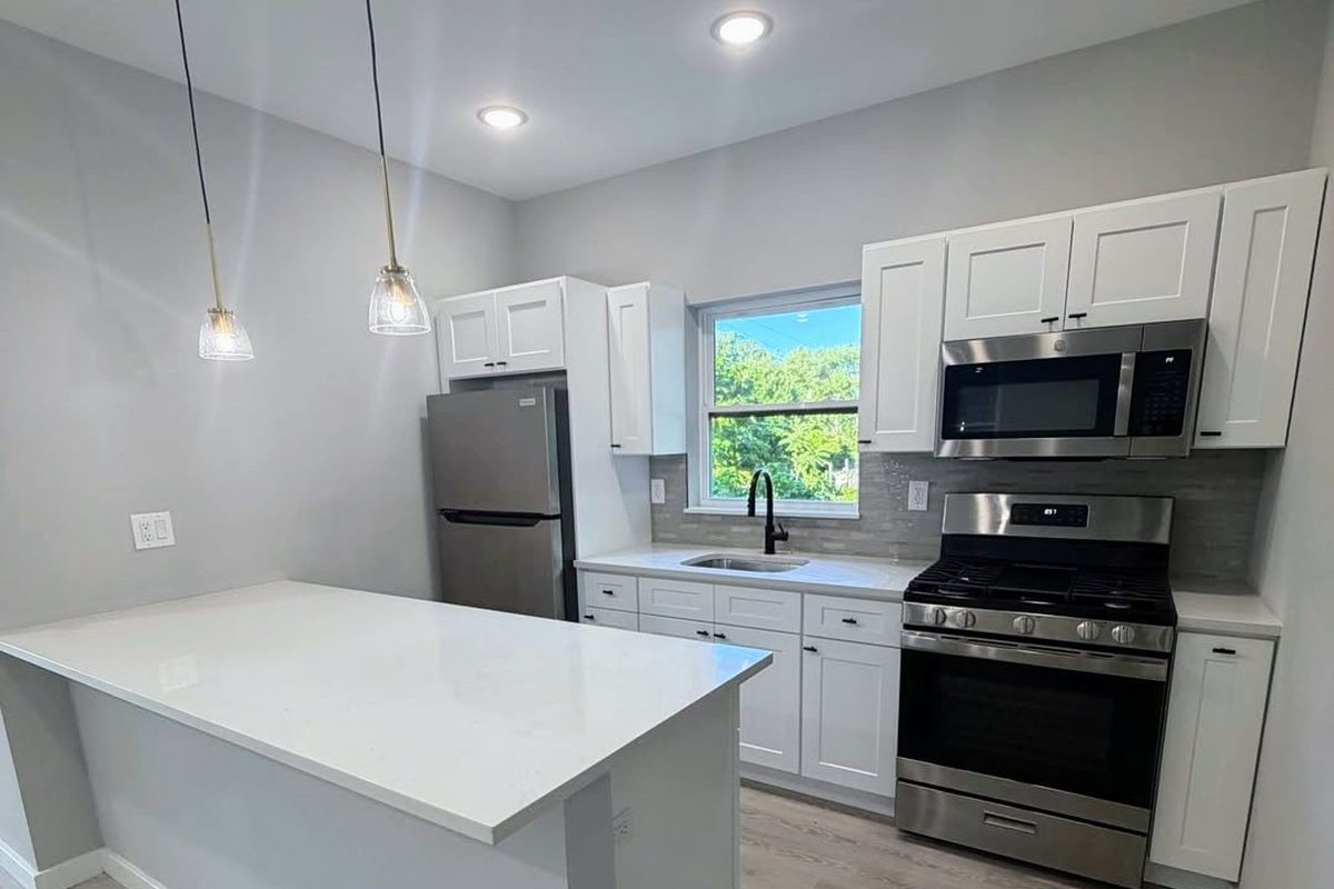 After: finished Pelham Parkway Bronx kitchen with white shaker cabinets, quartz peninsula, stainless steel appliances and light wood-look flooring