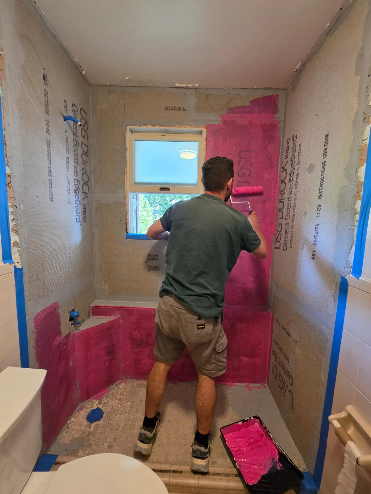 Contractor rolling waterproofing membrane onto cement board shower walls during a New York bathroom remodel
