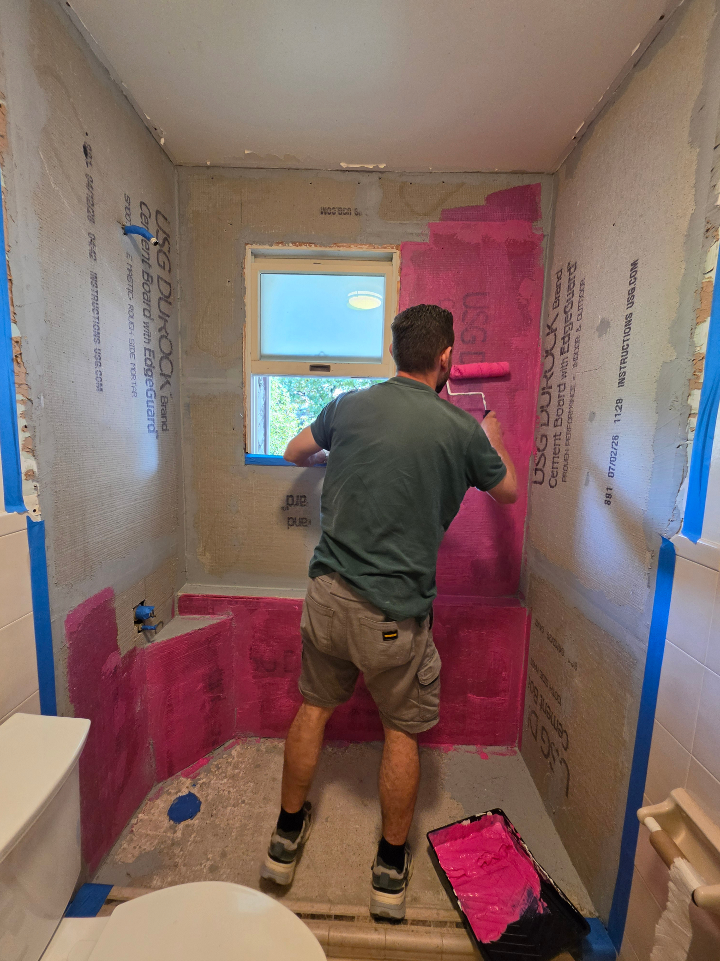 Contractor rolling waterproofing membrane onto cement board shower walls during a New York bathroom remodel