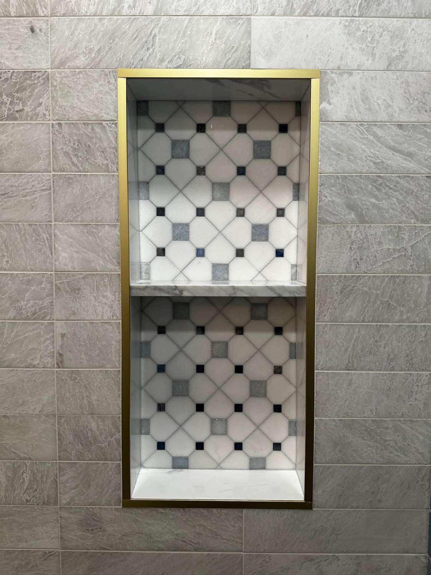 Brass-framed double shower niche with marble mosaic backing on grey stone tile, New York bathroom remodel