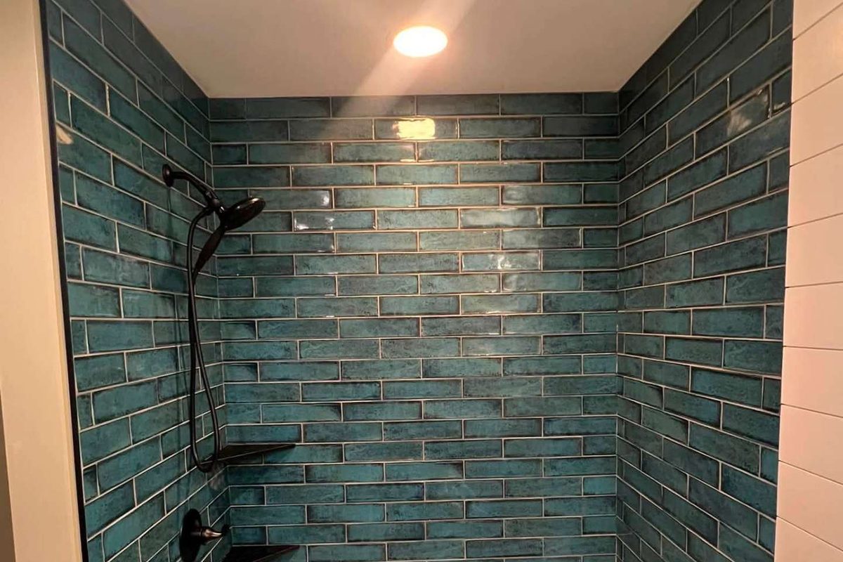 After: finished Morris Park Bronx bathroom with glossy teal subway tile shower surround, white soaking tub and matte black shower fixtures