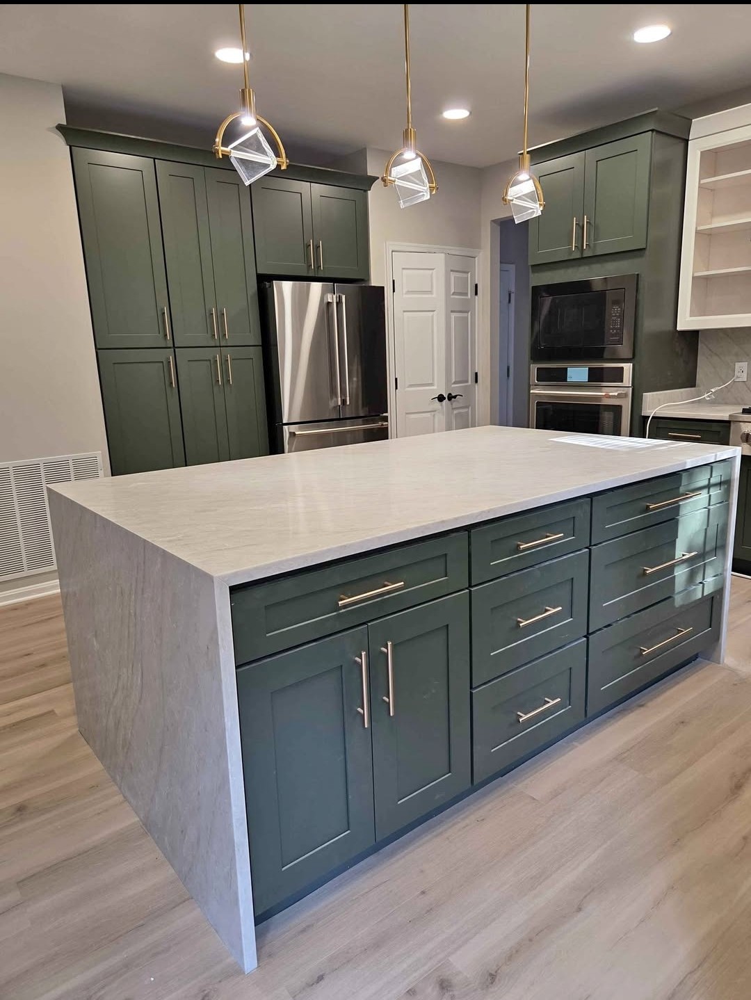 Deep green shaker kitchen with waterfall quartz island, gold pendant lights and stainless appliances