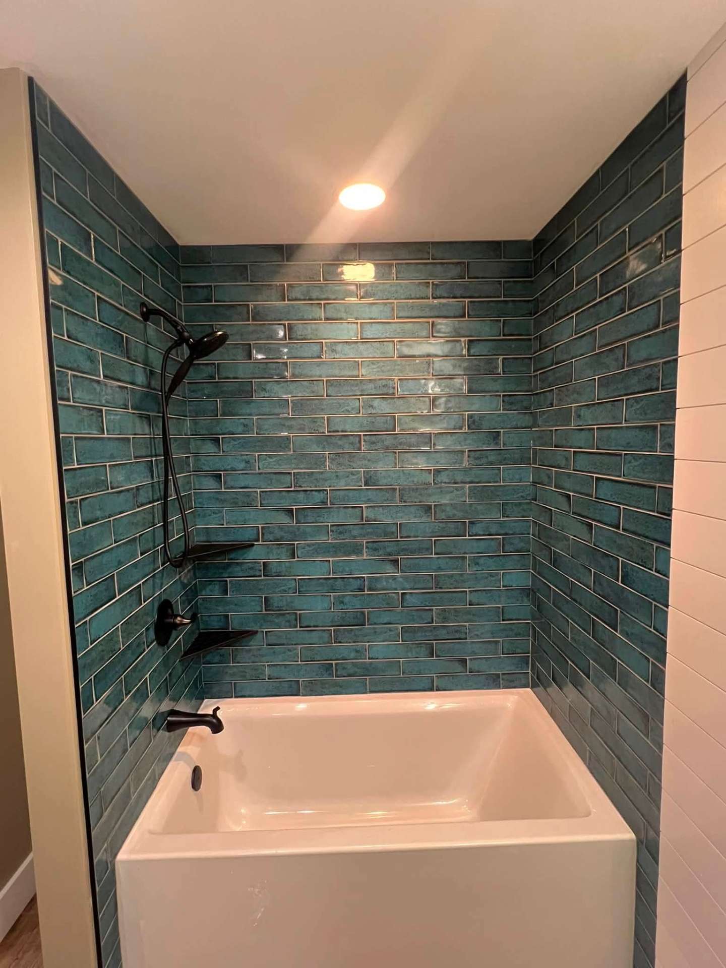 Tub and shower surround with glossy teal subway tile and matte black fixtures, NYC bathroom renovation