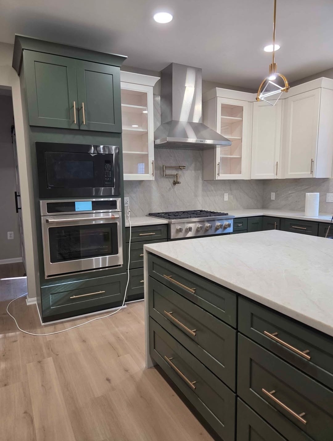 Green and white two-tone kitchen with marble backsplash, pot filler and stainless range hood